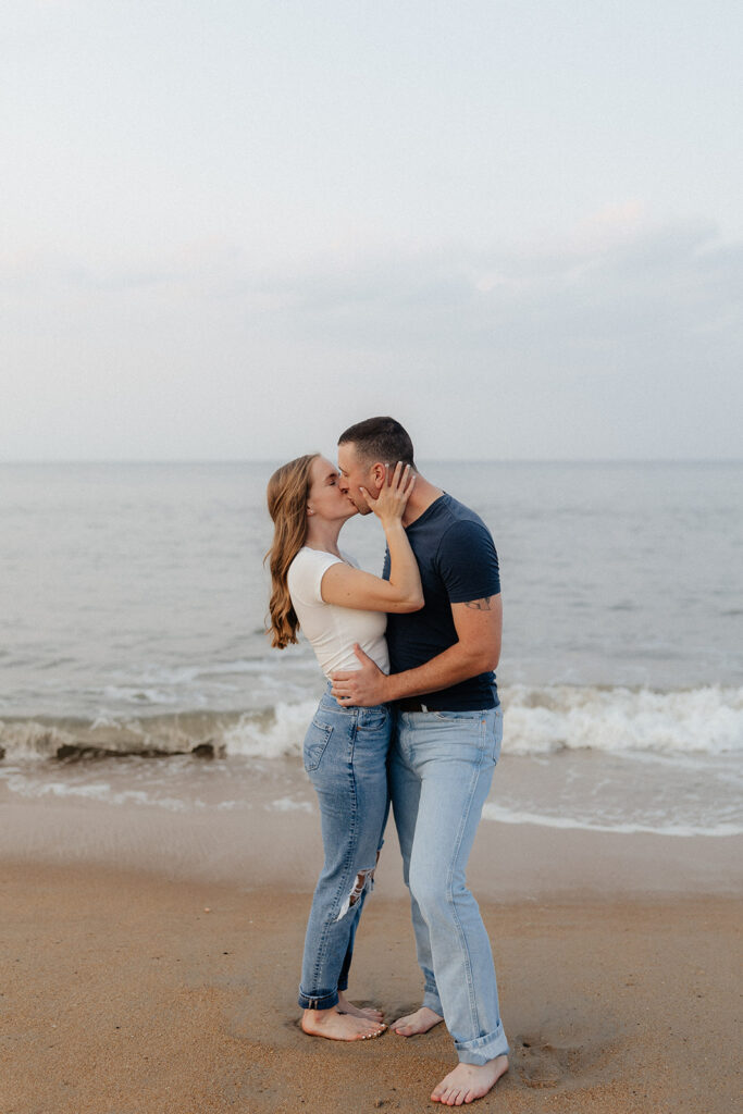 Destination elopement photographer captures newly engaged couple kissing on beach before destination elopement