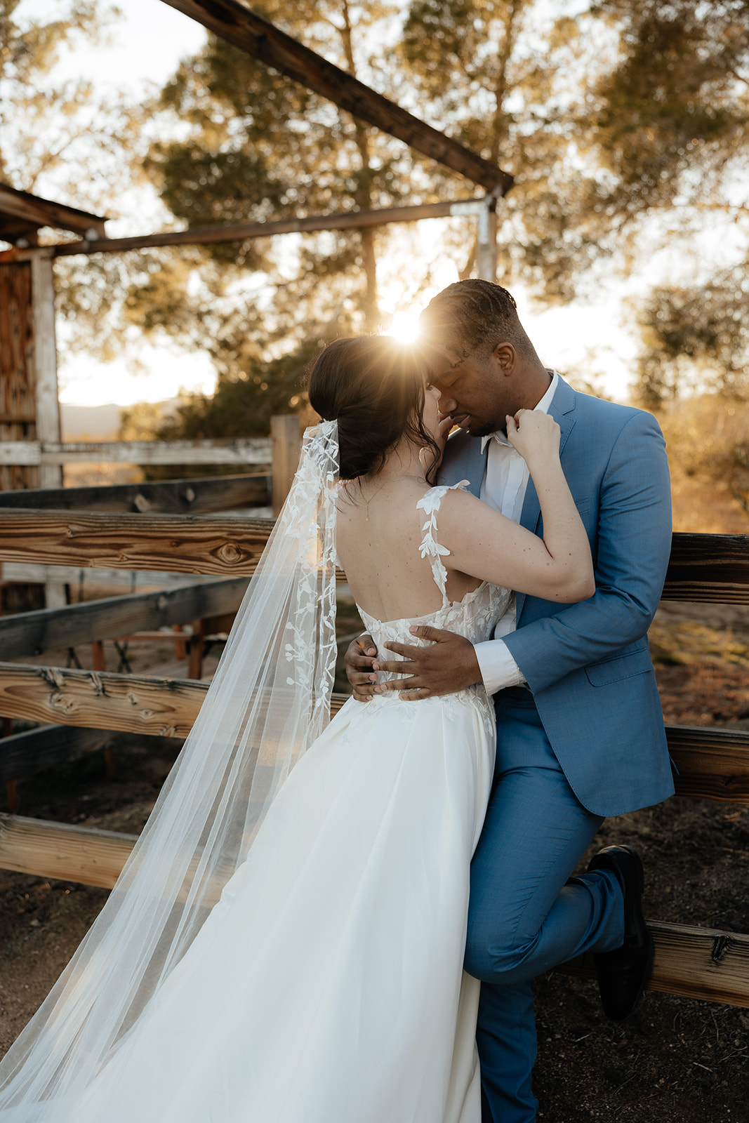 Destination elopement photographer captures bride and groom leaning against fence during golden hour for bridal portraits