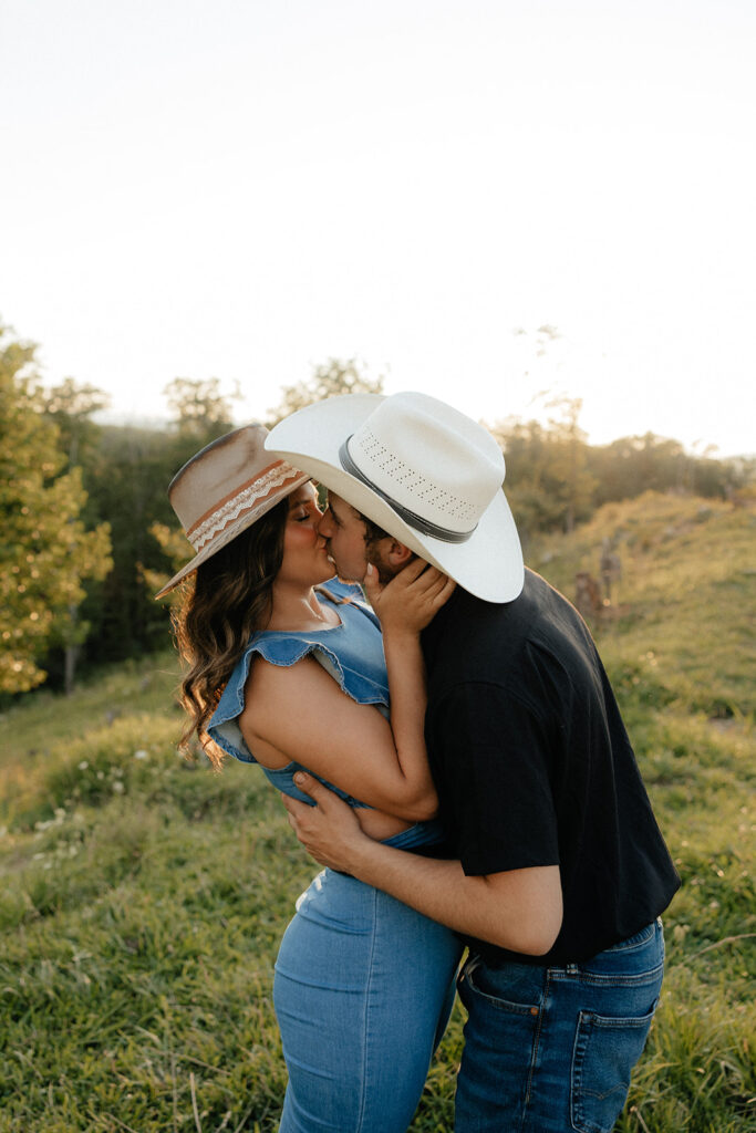 Tennessee elopement photographer captures couple kissing during western-inspired mountain engagement photos wearing cowboy hats